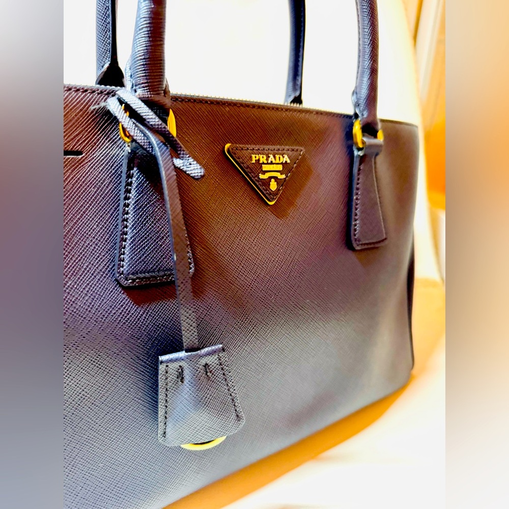 Authentic Prada, top-handle bag features a geometric shapemade of shiny leather.